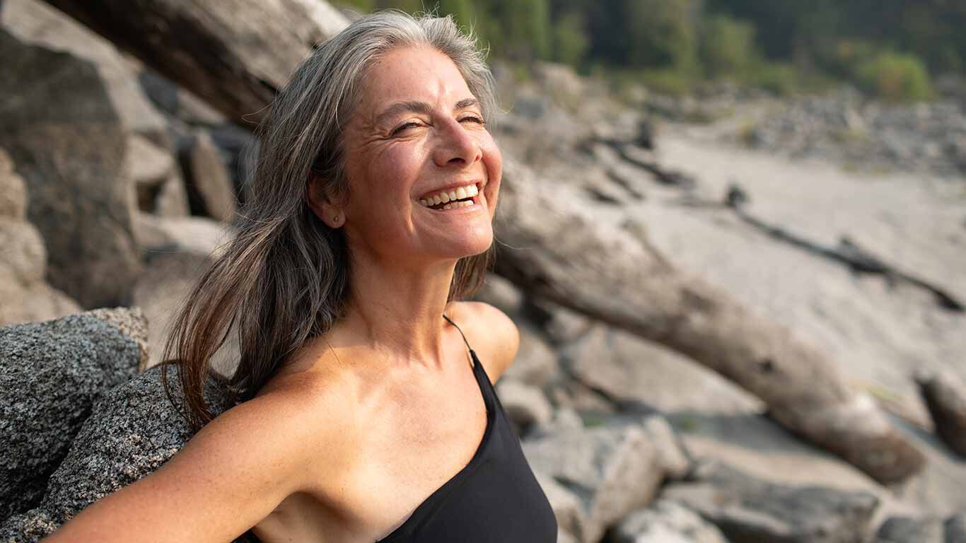 Femme âgée devant une paroi rocheuse en top, riant.